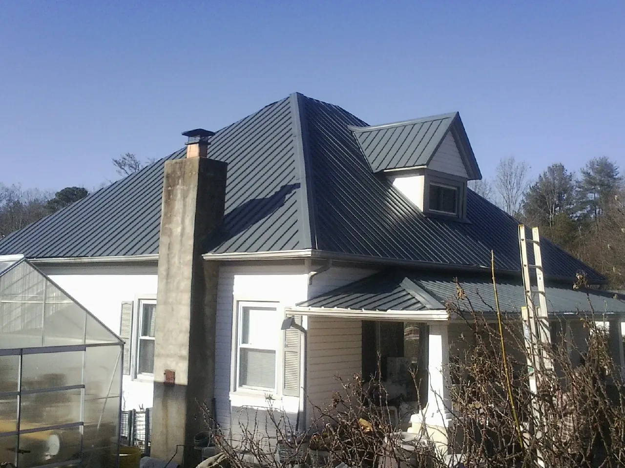 Dark blue standing seam metal roof on a white farmhouse with dormer — Slate & Tile Roof Repair by Roofing Brothers in Burgin