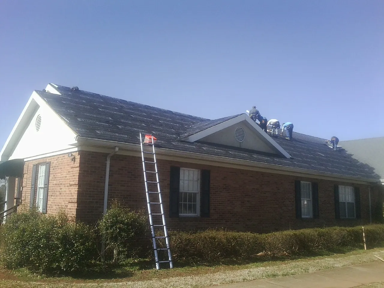 Crew tearing shingles off a brick ranch roof with a ladder set — Metal Roof Repair work by our crew in Burgin