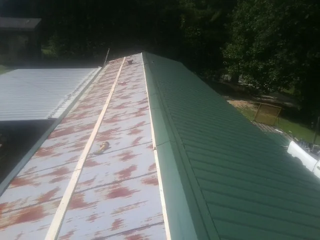 Old rusted panels beside newly installed green metal roofing — Wind Damage Roof Repair by Roofing Brothers in Burgin