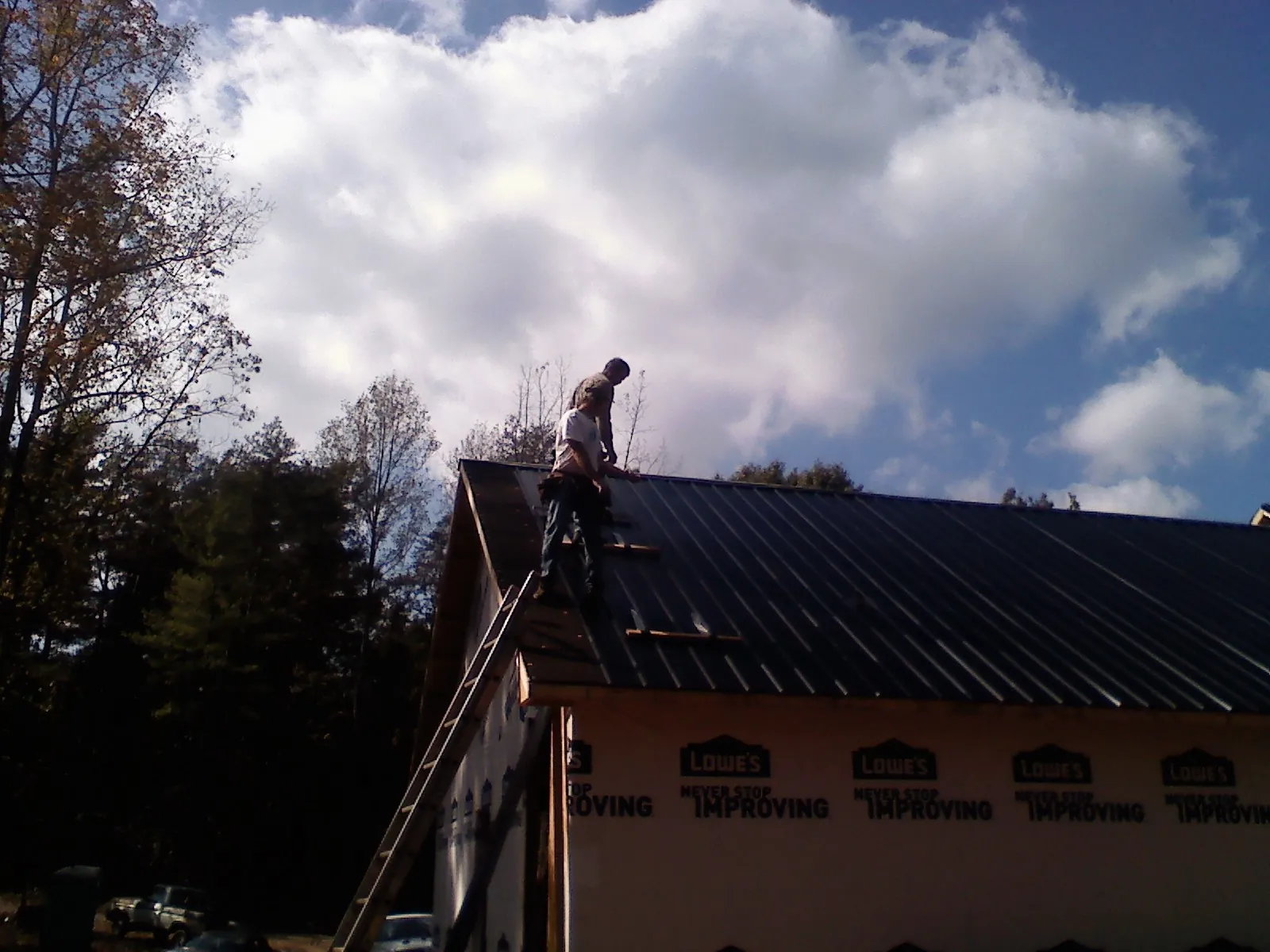 Roofer fastening dark metal panels high against a cloudy sky, from a Roof Inspection job in Burgin